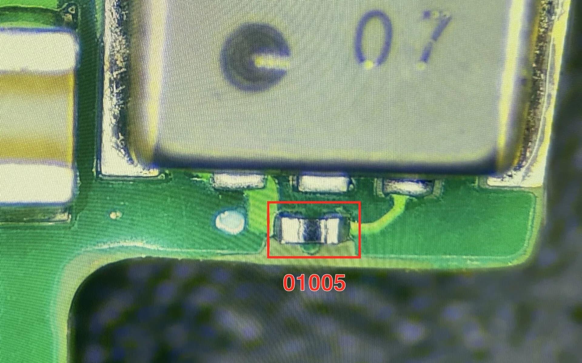 01005 komponentas, sumontuotas ir prilituotas ant gamybinės PCB plokštės, pro mikroskopą
